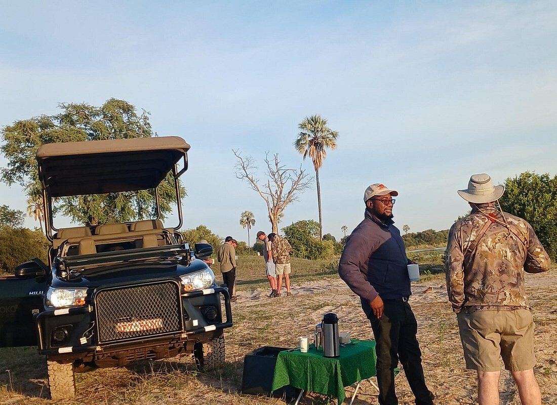Guide pouring coffee at a bush stop while guests stand beside the vehicle