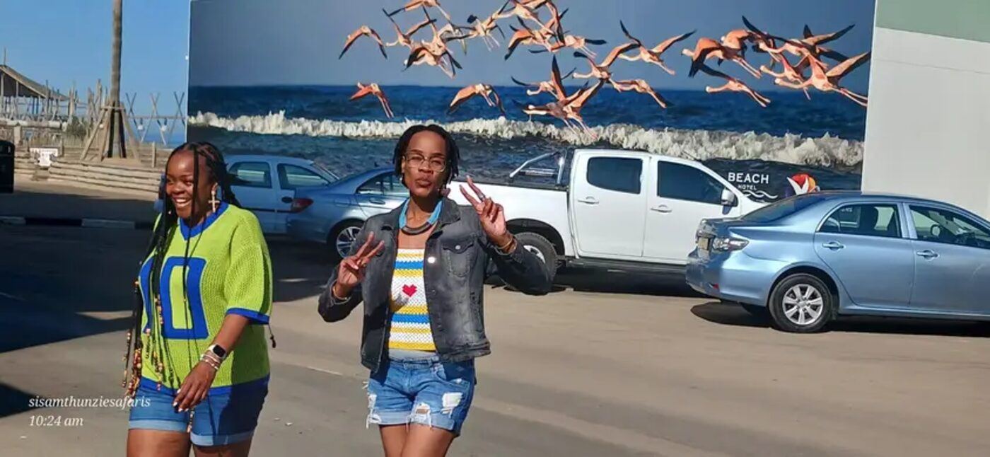 Two guests walking past a large flamingo mural on a coastal street
