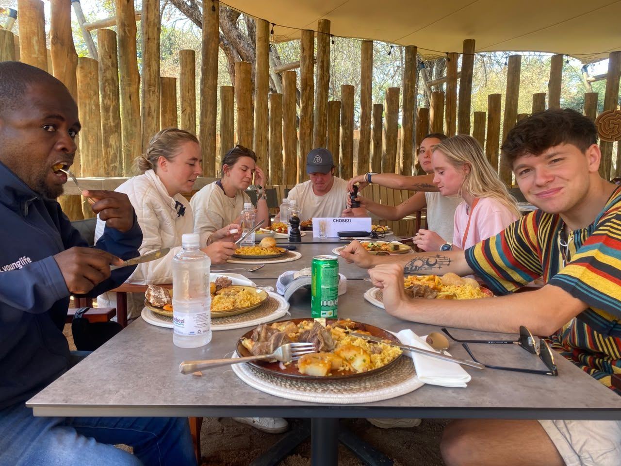 Guests sharing lunch at a long table under a thatched safari shelter