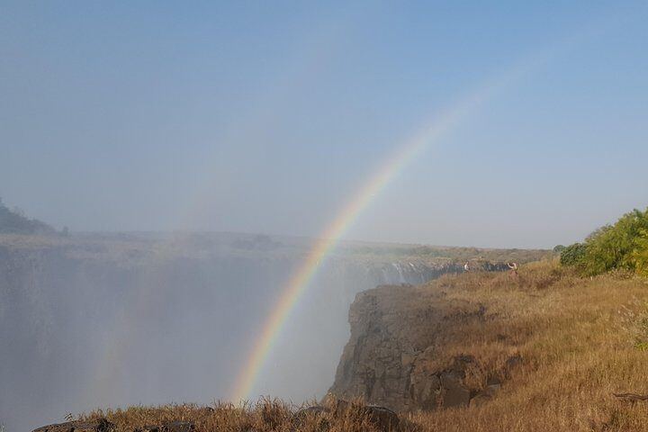 Rainbow arching over the grassy cliff edge above the Victoria Falls gorge